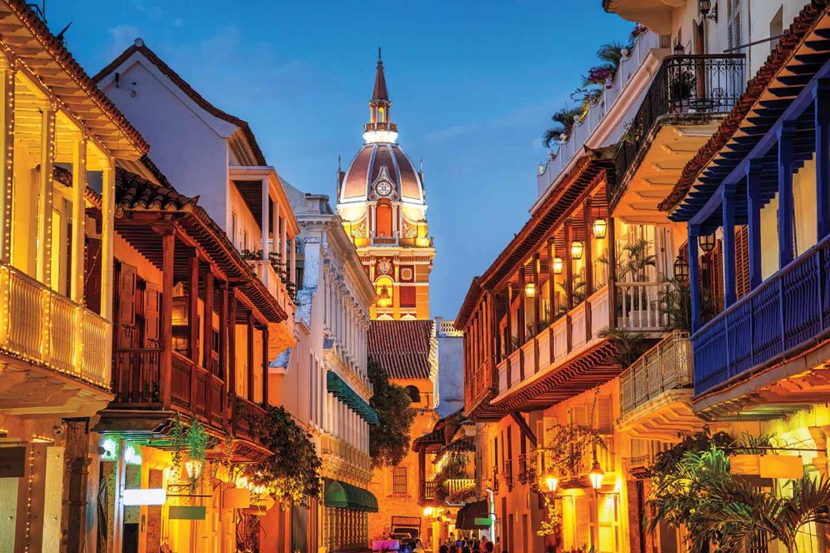 Calle de Cartagena al atardecer, con balcones y una torre iluminada.