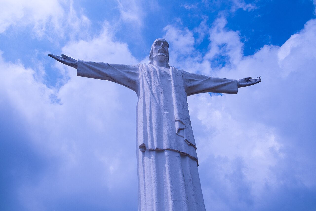 Cristo Rey en Cali, con los brazos abiertos bajo un cielo azul y nubes.